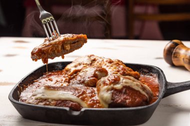 ahşap beyaz arka plan, peynir ve domates sosu üzerinde siyah demir tavada Filet Parmegiana olarak da bilinen parmegiana Steak açı görünümü