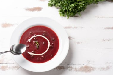 Beyaz ahşap masa arka planda beyaz bir tabakta ekşi krema ile lezzetli pancar çorbası