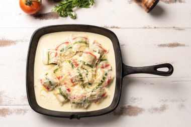 ahşap beyaz masa arka plan üzerinde, siyah demir tavada çok renkli ravioli makarna üst görünümü. 