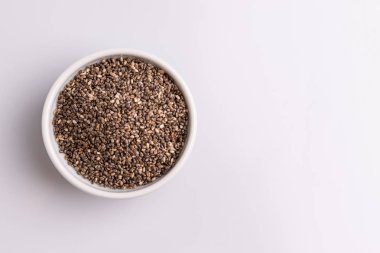 Topraklı chia tohumu (Salvia hispanica) beyaz bir seramik kase, beyaz arka plan üzerinde izole