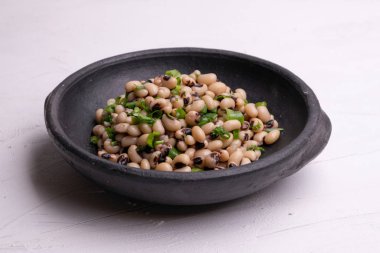 Beyaz arka plan üzerinde izole siyah kil tencerede pişmiş fradinho fasulye salatası,.