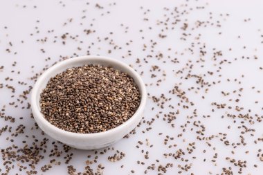 Topraklı chia tohumu (Salvia hispanica) beyaz bir seramik kase, beyaz arka plan üzerinde izole