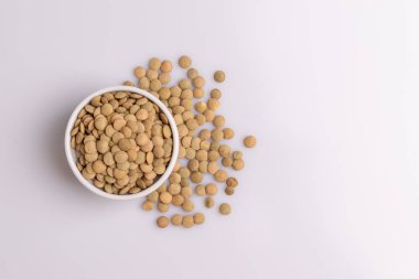 Beyaz bir seramik kase içinde kuru pişmemiş mercimek üst görünümü, beyaz arka plan üzerinde izole