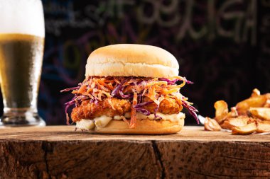 Rustik patates kızartması ve serin bir bardak bira ile ahşap rustik masada Cajun Coleslaw closeup ile Taze Gurme Tavuk Burger. Koyu arka plan 