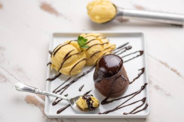 Beyaz ahşap arka plan üzerinde beyaz bir tabak vanilyalı dondurma ve çikolata sosu ile Petit gateau.