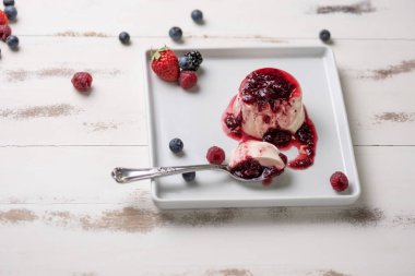 Berry soslu lezzetli İtalyan tatlı panna cotta, beyaz ahşap arka plan taze çilek