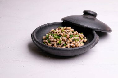Beyaz arka plan üzerinde izole siyah kil tencerede pişmiş fradinho fasulye salatası,.