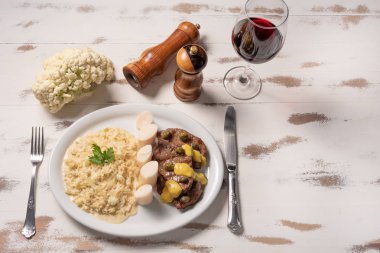 Fileto mignon ile Risotto. Ahşap beyaz arka plan üzerinde beyaz bir tabak ta kapari ve hardal ile Risoto ve sığır eti.