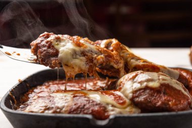 ahşap beyaz arka plan, peynir ve domates sosu üzerinde siyah demir tavada Filet Parmegiana olarak da bilinen parmegiana Steak açı görünümü