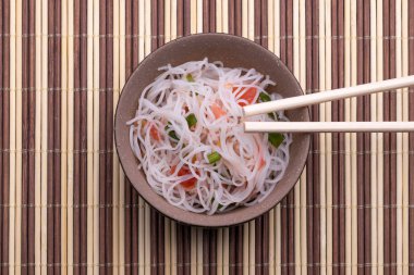 Pirinç erişte ve sebze ile Asya salatası. Pişmiş pirinç şehriye Tayland tarzı ahşap arka plan üzerinde izole çubukları ile siyah ve bronw kase