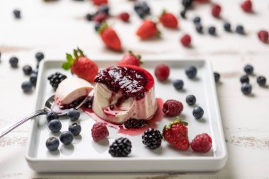 Berry soslu lezzetli İtalyan tatlı panna cotta, beyaz ahşap arka plan taze çilek