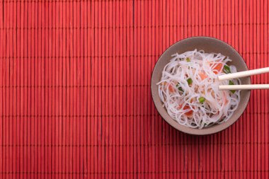 Pirinç erişte ve sebze ile Asya salatası. Kırmızı ahşap arka plan üzerinde izole siyah ve kahverengi bir kase pişmiş pirinç şehriye Tay tarzı. 