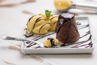 Beyaz ahşap arka plan üzerinde beyaz bir tabak vanilyalı dondurma ve çikolata sosu ile Petit gateau.