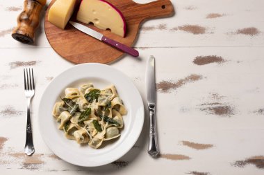 Beyaz ahşap masa arka plan üzerinde beyaz bir tabak tereyağı ve adaçayı ile ev yapımı tortellini.