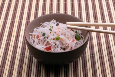 Pirinç erişte ve sebze ile Asya salatası. Pişmiş pirinç şehriye Tayland tarzı ahşap arka plan üzerinde izole çubukları ile siyah ve bronw kase