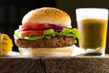 Hamburger, sığır eti, domates, soğan marulu, koçanda mısır, ahşap arka planda, açılı görüş, yumuşak ışık, stüdyo çekimi 