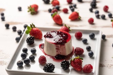 Berry soslu lezzetli İtalyan tatlı panna cotta, beyaz ahşap arka plan taze çilek