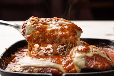 ahşap beyaz arka plan, peynir ve domates sosu üzerinde siyah demir tavada Filet Parmegiana olarak da bilinen parmegiana Steak açı görünümü