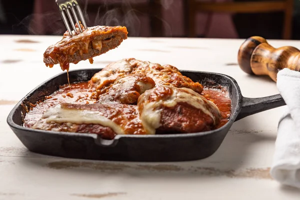 ahşap beyaz arka plan, peynir ve domates sosu üzerinde siyah demir tavada Filet Parmegiana olarak da bilinen parmegiana Steak açı görünümü