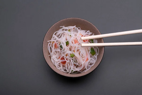 Cooked rice noodle Thai style in a black and bronw bowl with chopsticks isolated on gray background