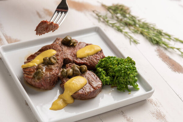 Filet mignon with caper and mustard sauce, broccoli, pepper grinder on wooden white background