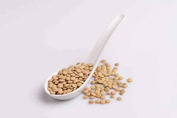 白いセラミックスプーンで乾燥した未調理のレンズ豆の角度図 白い背景に隔離 — ストック写真