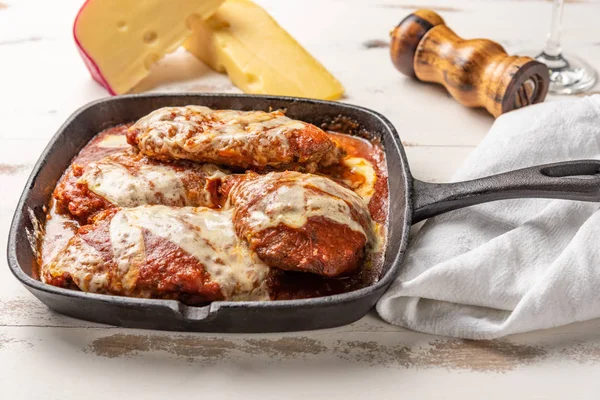 ahşap beyaz arka plan, peynir ve domates sosu üzerinde siyah demir tavada Filet Parmegiana olarak da bilinen parmegiana Steak açı görünümü