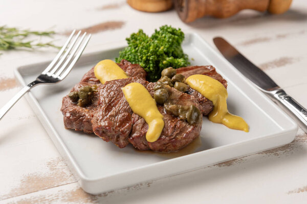 Filet mignon with caper and mustard sauce, broccoli, pepper grinder on wooden white background