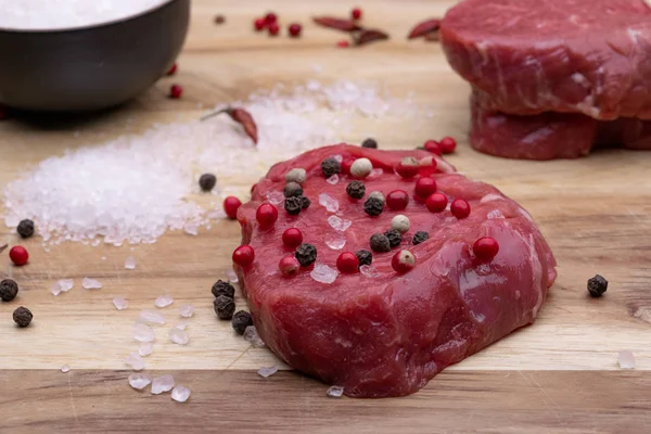 Raw beef fillet steaks with spices on wooden background, soft light, angle view