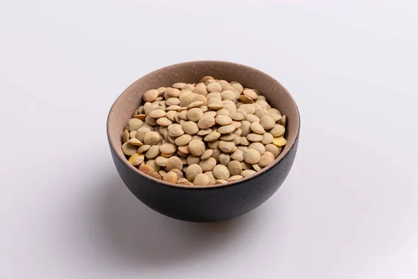 白い背景に隔離された黒いセラミックボウルの乾燥未調理のレンズ豆の角度図 — ストック写真