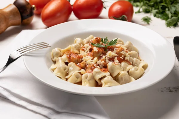 İtalyan tortellini (capeletti, agnolini) rustik beyaz ahşap masa arka plan üzerinde beyaz bir tabak domates sosu ile