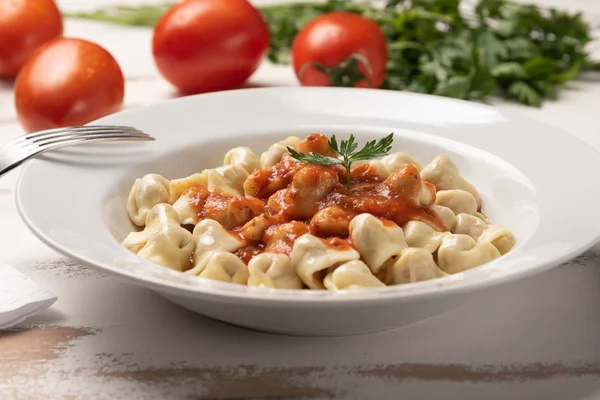 İtalyan tortellini (capeletti, agnolini) rustik beyaz ahşap masa arka plan üzerinde beyaz bir tabak domates sosu ile