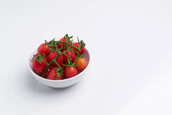 Angle view of grape or cherry tomatoes branch. Pile of red grape tomatoes in white bowl, isolated on white background