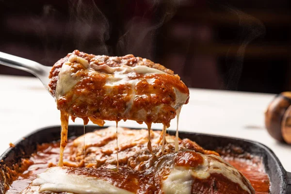 ahşap beyaz arka plan, peynir ve domates sosu üzerinde siyah demir tavada Filet Parmegiana olarak da bilinen parmegiana Steak açı görünümü