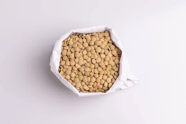 白い背景に隔離された白い紙袋の乾燥した未調理のレンズ豆のトップビュー — ストック写真