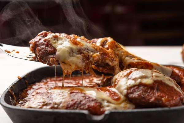 ahşap beyaz arka plan, peynir ve domates sosu üzerinde siyah demir tavada Filet Parmegiana olarak da bilinen parmegiana Steak açı görünümü