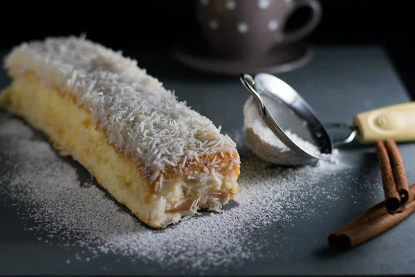 coconut sponge cake on black background, confectioner\'s sugar on surface and in a sieve