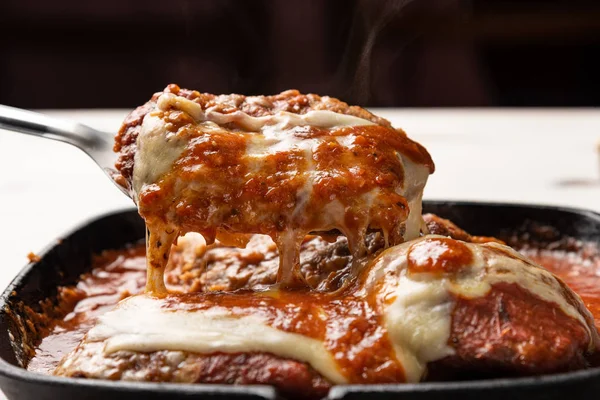 ahşap beyaz arka plan, peynir ve domates sosu üzerinde siyah demir tavada Filet Parmegiana olarak da bilinen parmegiana Steak açı görünümü