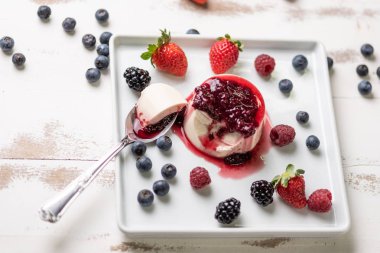 Berry soslu lezzetli İtalyan tatlı panna cotta, beyaz ahşap arka plan taze çilek