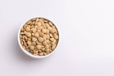 Beyaz bir seramik kase içinde kuru pişmemiş mercimek üst görünümü, beyaz arka plan üzerinde izole