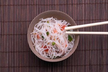 Pirinç erişte ve sebze ile Asya salatası. Pişmiş pirinç şehriye Tayland tarzı ahşap arka plan üzerinde izole çubukları ile siyah ve bronw kase
