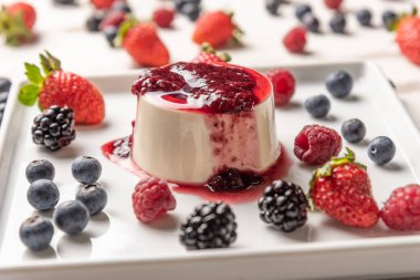 Berry soslu lezzetli İtalyan tatlı panna cotta, beyaz ahşap arka plan taze çilek