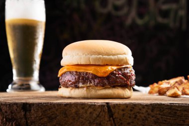 Rustik patates kızartması ve serin bir bardak bira ile ahşap rustik masada taze burger closeup. Lezzetli çizburger. Ev yapımı hamburger, biftek ve peynir. Koyu arka plan 