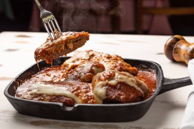 ahşap beyaz arka plan, peynir ve domates sosu üzerinde siyah demir tavada Filet Parmegiana olarak da bilinen parmegiana Steak açı görünümü