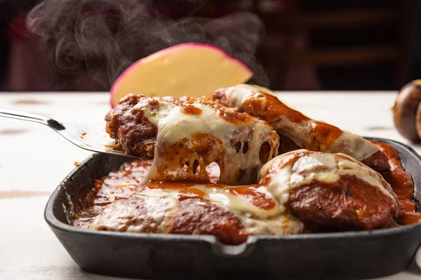 ahşap beyaz arka plan, peynir ve domates sosu üzerinde siyah demir tavada Filet Parmegiana olarak da bilinen parmegiana Steak açı görünümü