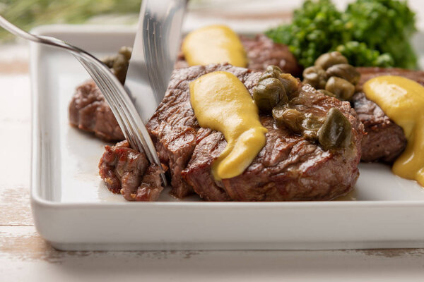 Filet mignon with caper and mustard sauce, broccoli, pepper grinder on wooden white background