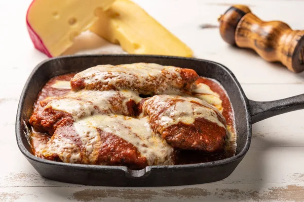ahşap beyaz arka plan, peynir ve domates sosu üzerinde siyah demir tavada Filet Parmegiana olarak da bilinen parmegiana Steak açı görünümü