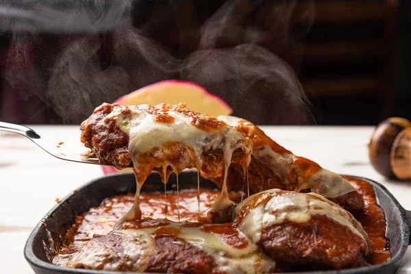 在木制白色背景 奶酪和番茄酱的黑色铁锅中 可观的帕美吉亚牛排也被称为 Filet Parmegiana — 图库照片