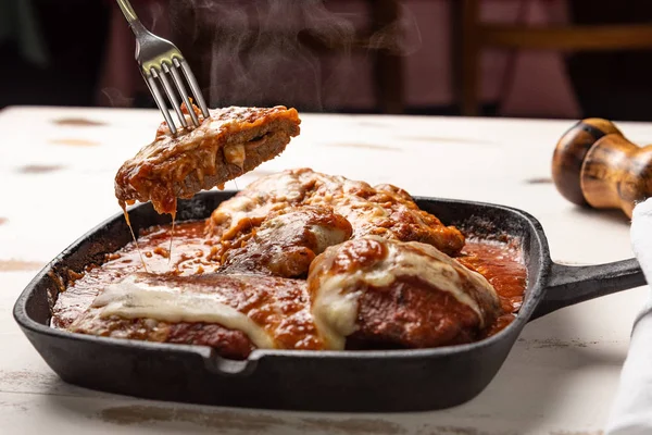 ahşap beyaz arka plan, peynir ve domates sosu üzerinde siyah demir tavada Filet Parmegiana olarak da bilinen parmegiana Steak açı görünümü