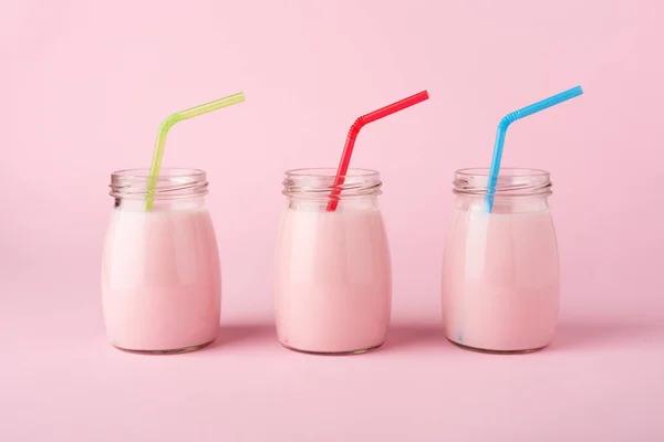 三瓶水果酸奶与彩色吸管在柔和的粉红色背景 最小的样式 侧面视图 健康的生活方式 — 图库照片